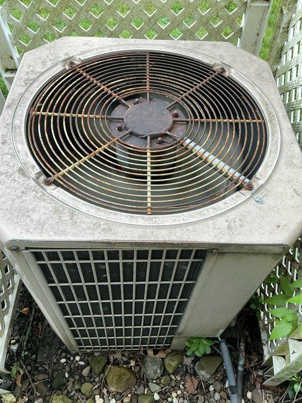 Responded to service call for air conditioning unit not cooling. Upon inspection, found outdoor condenser unit showing significant age and weathering with visible rust on fan grille and algae growth on exterior panels. Performed diagnostic assessment of both outdoor condenser and indoor air handler components to identify cooling system failure.