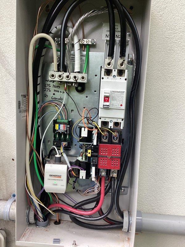 # Electrical Install - Generator

Completed installation of an 18kW Generac standby generator system with full electrical integration. Mounted and wired automatic transfer switch (ATS) within new service panel enclosure, establishing proper connections between utility service, generator output, and load center distribution. Installed 200-amp rated disconnect with appropriate overcurrent protection and safety interlocks.

Performed complete panel wiring including:
- Main utility feed connections with proper phase identification
- Generator input wiring to ATS with correct conductor sizing
- Load side distribution to existing electrical service
- Grounding and bonding of all components per NEC requirements
- Installation of Generac control module with status indicators
- Terminal block configuration for multiple circuit integration

Verified proper wire routing and strain relief for all black, white, red, and green conductors entering top and bottom of enclosure. Secured all connections 