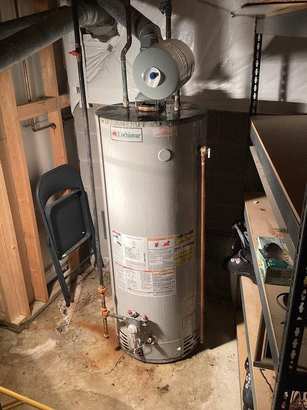 Responded to no hot water call and inspected Lochinvar residential water heater system in utility room. Identified moisture accumulation on galvanized piping and verified all plumbing connections, shut-off valves, copper piping, expansion tank, and safety components were functioning properly. System restored to normal operation with hot water service confirmed.