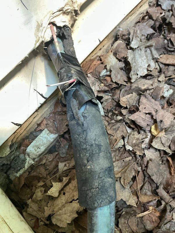 # HVAC Service Call - No Cooling Follow-Up

Responded to no cooling complaint on system that was not operating. This was a follow-up visit to a previous service call completed two weeks prior. Upon arrival, conducted visual inspection of outdoor condensing unit and associated refrigerant lines.

Exterior inspection revealed outdoor unit surrounded by significant leaf debris accumulation around the foundation area. Noted deteriorated insulation on refrigerant line set near building exterior, with yellow foam insulation showing signs of crumbling and damage. Line set insulation was compromised with exposed sections visible along the vertical run near the foundation.

Observed condensing unit location with multiple utility lines and cables running along ground level. Unit appeared accessible but surrounded by organic debris that could potentially restrict airflow or cause operational issues. Photographed equipment location and condition of refrigerant lines for documentation purposes.

Sy
