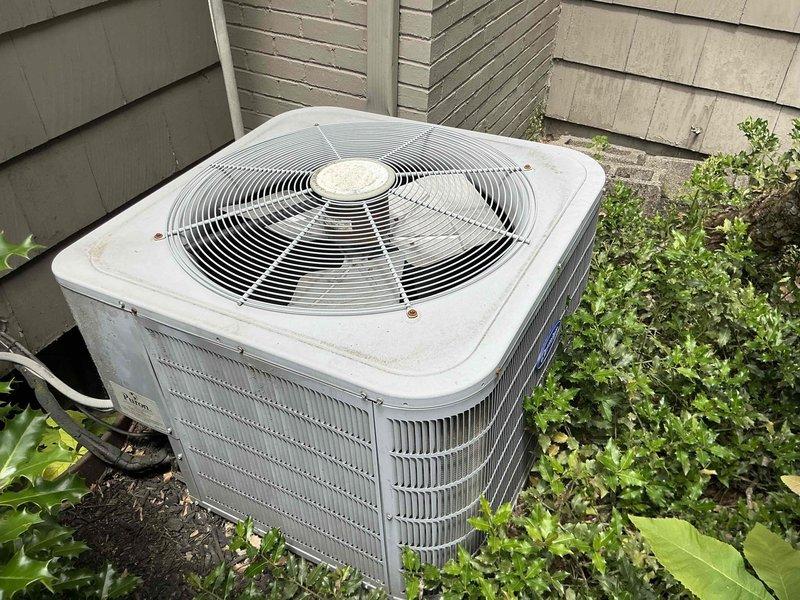 Conducted on-site evaluation of existing outdoor air conditioning condenser unit for replacement estimate. Unit displayed weathered exterior surfaces with visible discoloration and signs of prolonged outdoor exposure. Assessed surrounding conditions including overgrown vegetation encroaching on equipment, which may restrict proper airflow and reduce system efficiency. Documented current equipment specifications, installation location against exterior wall with mixed siding types, and accessibility for replacement work. Photographed existing unit positioning, clearance requirements, and electrical connections to provide comprehensive replacement options for customer consideration.