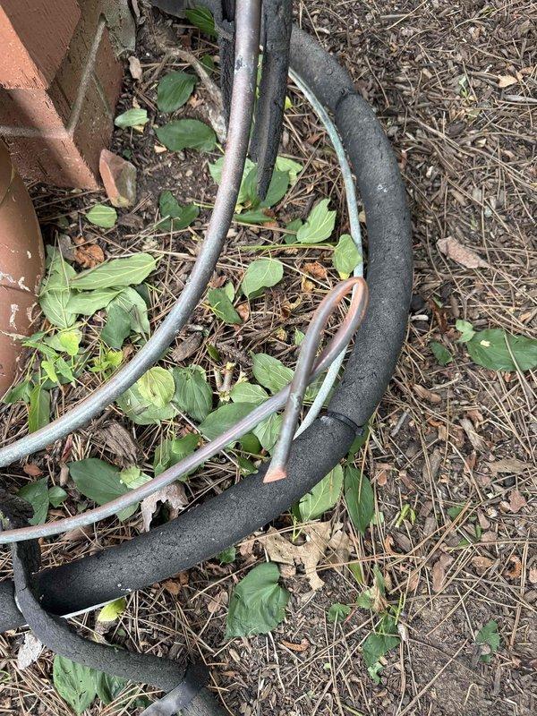 Responded to service call for damaged refrigerant line that was accidentally severed during home renovation work. Upon arrival, inspected the exterior HVAC system consisting of two condenser units with refrigerant lines running along the building foundation. Documented the cut refrigerant line with deteriorated black foam insulation and assessed the extent of damage to the copper tubing. The compromised line required immediate attention to restore cooling system functionality and prevent further refrigerant loss.