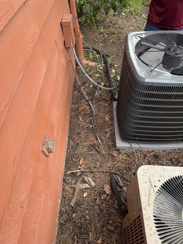 Responded to service call for damaged refrigerant line that was accidentally severed during home renovation work. Upon arrival, inspected the exterior HVAC system consisting of two condenser units with refrigerant lines running along the building foundation. Documented the cut refrigerant line with deteriorated black foam insulation and assessed the extent of damage to the copper tubing. The compromised line required immediate attention to restore cooling system functionality and prevent further refrigerant loss.
