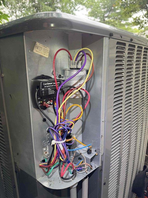Responded to service call for air conditioning unit producing abnormal loud noise. Upon arrival, performed visual inspection of outdoor condenser unit and accessed electrical compartment to diagnose issue. Removed access panel to examine internal components, wiring connections, and CoreSense monitoring module. Inspected all electrical connections, wire routing, and control systems for loose components or mechanical failures that could generate unusual sounds during operation. Unit assessed and findings documented with photographic evidence of equipment condition and internal configuration.