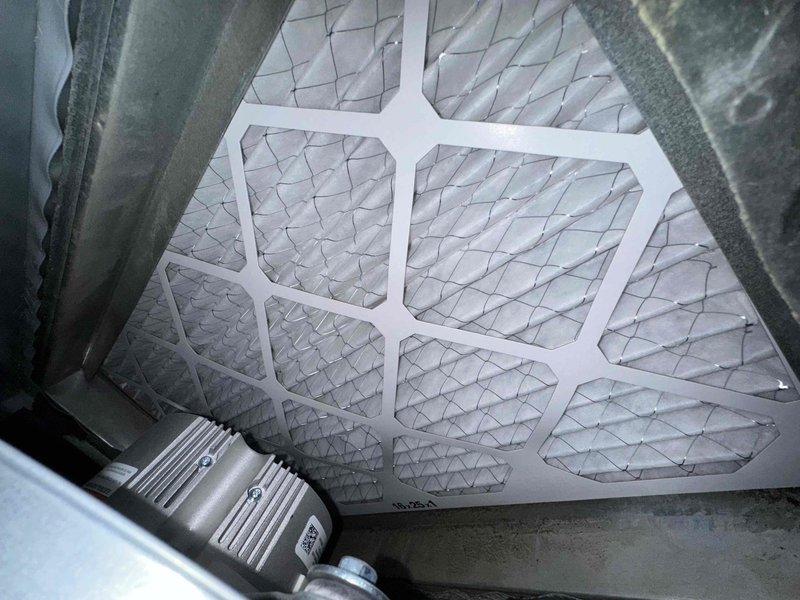 Performed comprehensive cooling system maintenance on HVAC unit. Inspected and documented air filter condition within the air handler, noting the pleated diamond mesh filter properly installed in the metal ductwork housing. Examined blower assembly components, including the centrifugal fan with radial blade configuration and central motor shaft, confirming proper mechanical operation and clearances within the blower housing.