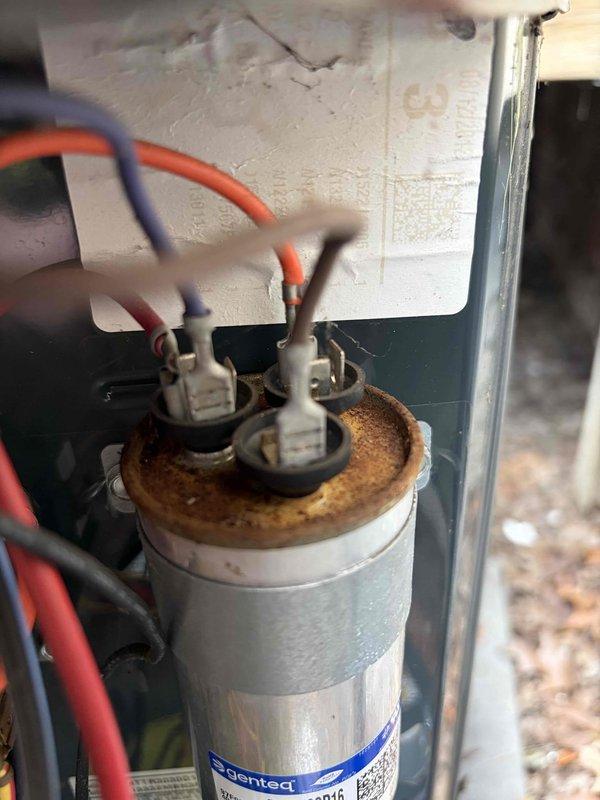 # HVAC Cooling Maintenance Completed

Performed routine preventive maintenance on residential split-system air conditioning unit located beneath elevated deck structure. Conducted comprehensive inspection of outdoor condenser unit, including visual assessment of cabinet condition, fan assembly, and protective grille. Verified proper placement on concrete pad and checked clearances around unit.

Opened electrical compartment and inspected internal components. Identified significant rust and corrosion on capacitor terminal cap, indicating moisture intrusion and potential component degradation. Corrosion was concentrated around terminal connections on top of dual-run capacitor. Noted wiring connections remained intact with red and gray/blue conductors properly terminated to capacitor posts.

Documented equipment condition through photographic documentation for maintenance records. Unit operational at time of service. Recommended monitoring capacitor performance and considering replacement