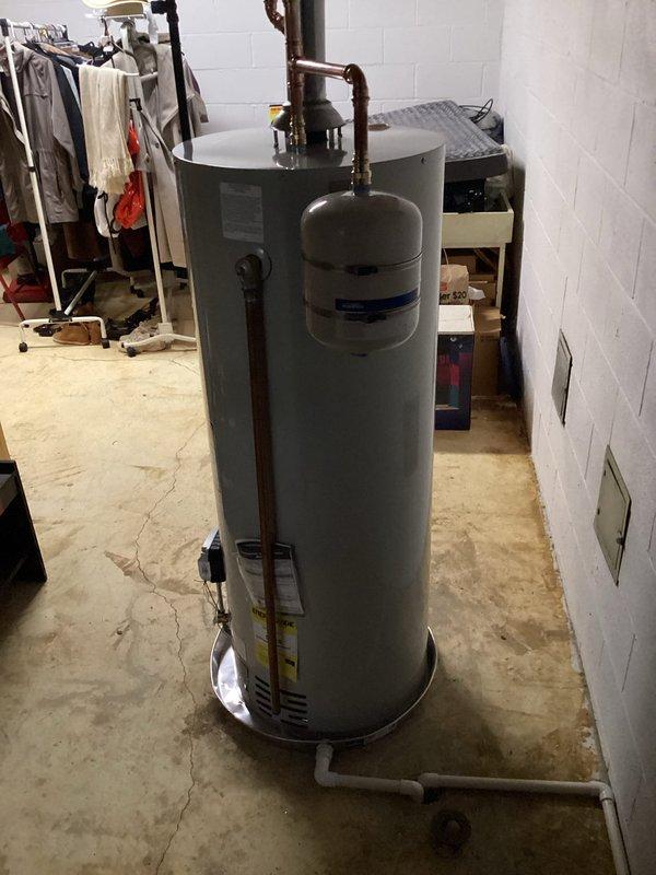 Replaced 50-gallon Bradford White residential water heater in basement utility area with complete installation including all current code-required upgrades. Installation included proper venting with metal flue pipe, copper supply line connections with shutoff valves, expansion tank mounting, and PVC discharge piping, ensuring system meets all local plumbing and safety code requirements.