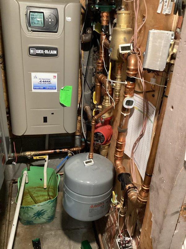 Responded to reported possible hot water system pipe leak at residential property with mechanical systems dating to 1969. Conducted thorough visual inspection of utility room containing Weil-McLain water heater, furnace unit, expansion tanks, and associated copper and PVC piping infrastructure. Examined all visible pipe connections, joints, valves, and fittings throughout the heating and domestic water distribution system for signs of active leakage, moisture accumulation, corrosion, or mineral deposits. Inspected pressure tank, expansion tank, and circulator pump assembly with red-handled valve for potential leak sources. Assessed condition of copper supply lines, return lines, and various brass fittings connecting system components. Photographed equipment configuration and piping layout for documentation purposes. No active leaks were identified during visual inspection of accessible mechanical equipment and piping at time of service call.