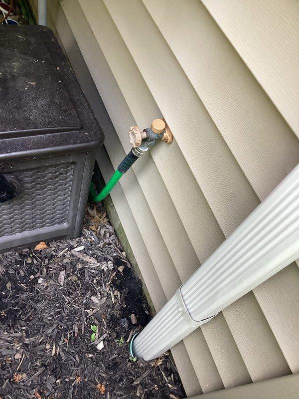 Responded to service call for exterior hose faucet requiring repair or replacement. Upon inspection, assessed the outdoor spigot connection mounted through vinyl siding and accessed the interior plumbing chase to examine water supply lines. Evaluated the brass fittings, PVC supply piping with blue shut-off valve, and connection points to determine necessary repairs and ensure proper functionality of the exterior hose bib system.