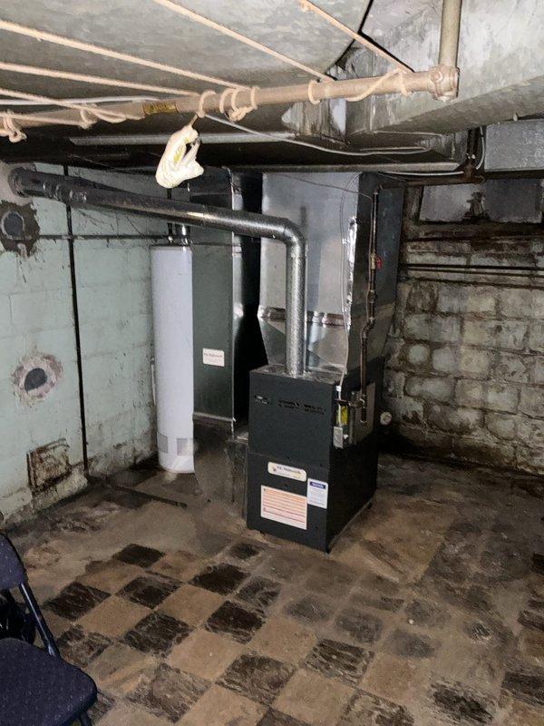 Completed HVAC estimate for air conditioning system replacement in residential property. Assessed existing basement mechanical room infrastructure, including electrical panels, ductwork configuration, and available space for new AC installation. Documented current conditions of utility area showing aged electrical systems, existing furnace with overhead ductwork, and water heater to determine compatibility and requirements for new cooling equipment integration with existing HVAC infrastructure.