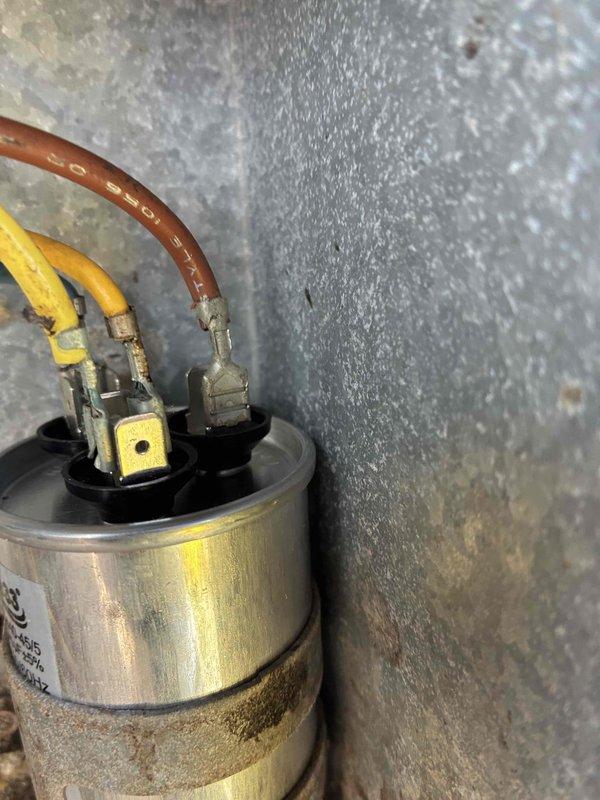 Responded to service call for window AC unit making noise but not cooling properly. Upon inspection, found heavily corroded capacitor with significant dirt and grime buildup, along with severely deteriorated condenser coil housing showing extensive rust, corrosion, and debris accumulation. Replaced failed capacitor, cleaned accessible components, and restored cooling operation to unit.