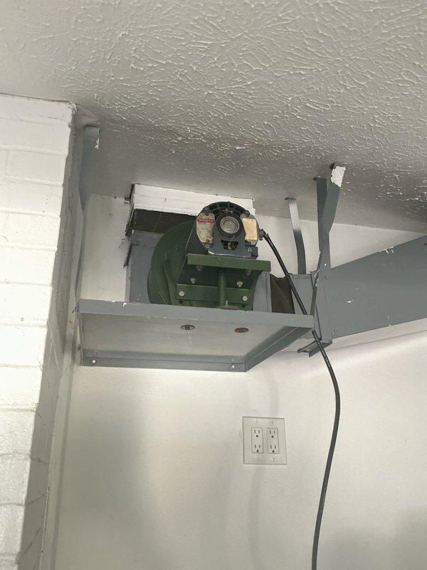 Conducted site assessment for exhaust fan installation estimate. Evaluated existing ventilation system mounted in utility space, documenting current blower assembly with light green metal housing and visible electrical wiring configuration. Inspected electrical service panel to verify available circuit capacity and breaker allocation for potential new exhaust fan installation. Photographed existing conditions including wall-mounted receptacles and ceiling texture to determine optimal mounting location and electrical routing requirements for proposed exhaust fan unit.