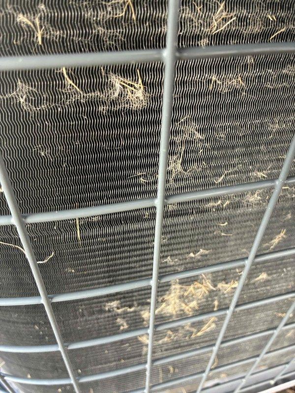 Performed follow-up inspection of air conditioning system after previous maintenance visit. Upon examination, found condenser coils had accumulated significant debris including dust, lint, and airborne particulates that were restricting airflow through the heat exchanger fins. Cleaned condenser coils thoroughly to remove all buildup and restore optimal system performance. Verified proper airflow through protective wire guard and confirmed unit is operating within normal parameters.