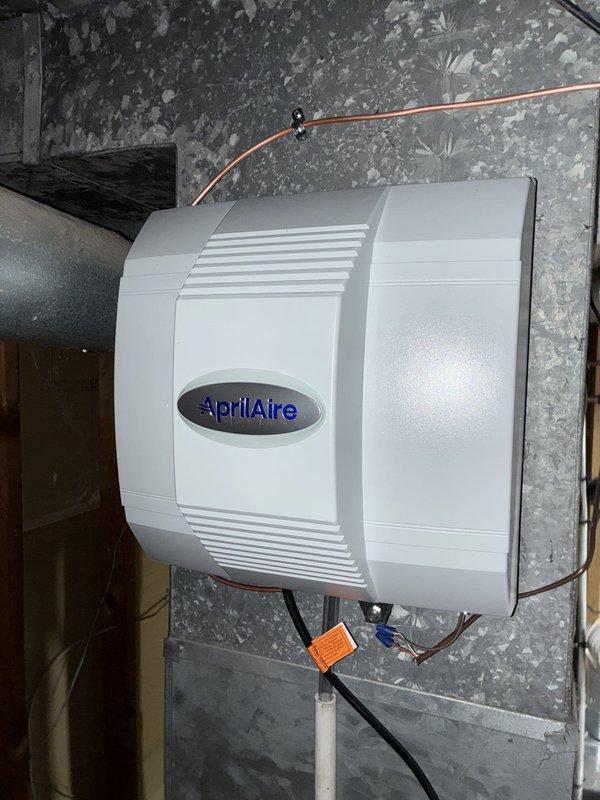Completed full HVAC system installation including 80% efficiency Goodman furnace, air conditioning unit, ductwork with liner, and AprilAire whole-home humidifier. Mounted furnace in basement utility area with proper clearances and ventilation. Installed black flexible ductwork connecting to supply and return plenums, with white return air grille properly positioned on wall. Connected metal flue pipe with elbow configuration for exhaust venting. Installed AprilAir humidifier unit on concrete block wall with copper water supply line secured with mounting clips, connected electrical wiring including power leads and control wiring with proper wire nuts and connectors. Integrated humidifier into HVAC ductwork system for whole-house humidity control. Completed all electrical connections per manufacturer specifications and local code requirements. Verified proper airflow, tested all system components for functionality, and ensured secure mounting of all equipment. System operational and ready