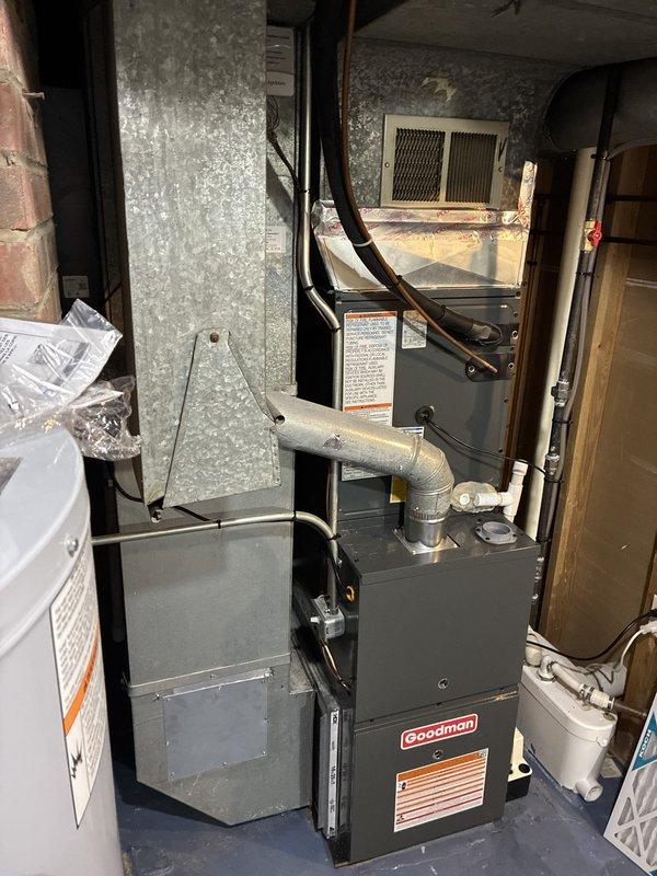 Completed full HVAC system installation including 80% efficiency Goodman furnace, air conditioning unit, ductwork with liner, and AprilAire whole-home humidifier. Mounted furnace in basement utility area with proper clearances and ventilation. Installed black flexible ductwork connecting to supply and return plenums, with white return air grille properly positioned on wall. Connected metal flue pipe with elbow configuration for exhaust venting. Installed AprilAir humidifier unit on concrete block wall with copper water supply line secured with mounting clips, connected electrical wiring including power leads and control wiring with proper wire nuts and connectors. Integrated humidifier into HVAC ductwork system for whole-house humidity control. Completed all electrical connections per manufacturer specifications and local code requirements. Verified proper airflow, tested all system components for functionality, and ensured secure mounting of all equipment. System operational and ready