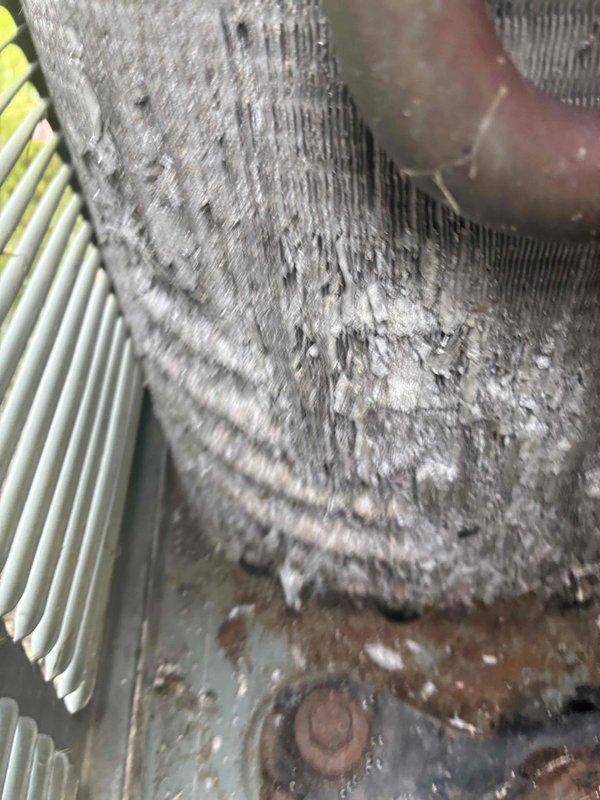 Performed HVAC maintenance service on air conditioning system. Upon inspection, found evaporator coils heavily contaminated with dust and debris buildup, significantly restricting airflow and reducing system efficiency. Coil fins showed extensive accumulation of particulate matter with matted, fuzzy appearance throughout. Identified corroded metal housing and base plate with visible rust spots. Refrigerant lines displayed oxidation and patina consistent with prolonged exposure to moisture. Observed mineral deposits and white/gray oxidation on heat exchanger fins with vertical streaking patterns indicating condensation issues. Air filter showed signs of requiring replacement. Cleaned evaporator coils thoroughly to restore proper airflow and heat transfer capability. Addressed corrosion concerns on copper refrigerant piping and system components. System restored to operational condition with improved efficiency.