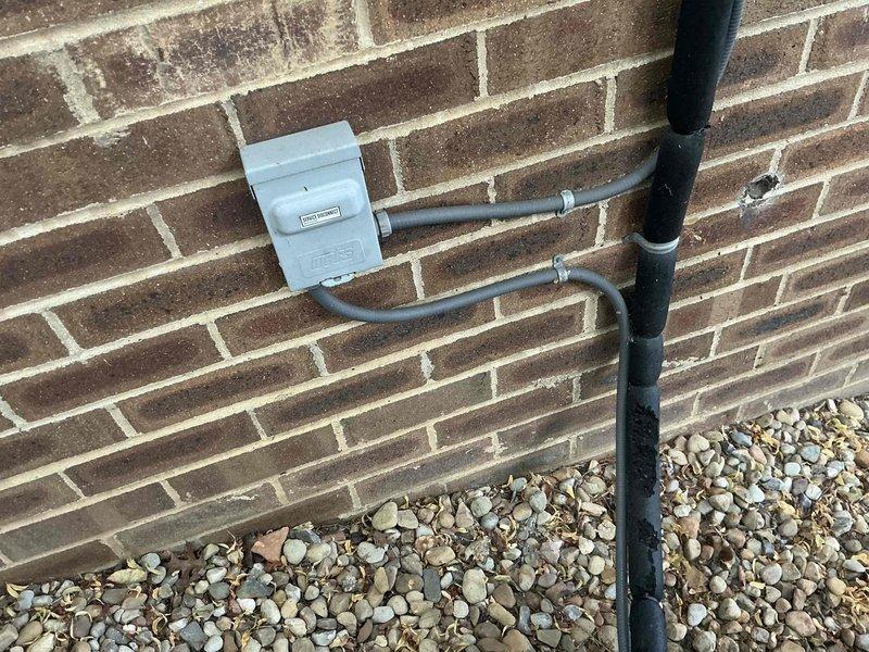 Provided replacement estimate options for existing residential air conditioning system at rental property. Evaluated current outdoor condensing unit positioned on gravel pad adjacent to building foundation and assessed electrical disconnect and conduit configuration mounted on exterior brick wall. Documented equipment condition and installation setup with photographs for property owner review and decision-making on replacement versus repair options.