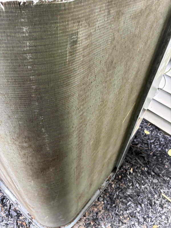 # HVAC Cooling Maintenance Completed

Performed routine preventive maintenance on residential air conditioning system as part of ongoing service agreement. Removed and inspected condensing unit cover, which displayed significant weathering, algae growth, and deterioration along top edge with jagged breaks in material. Accessed internal components by removing exterior shroud to inspect condenser coils, fins, and electrical connections. Documented equipment condition showing aged exterior panels with substantial environmental exposure, oxidation, and biological growth accumulation. Unit operational at time of service with all internal components accessible for standard maintenance procedures.