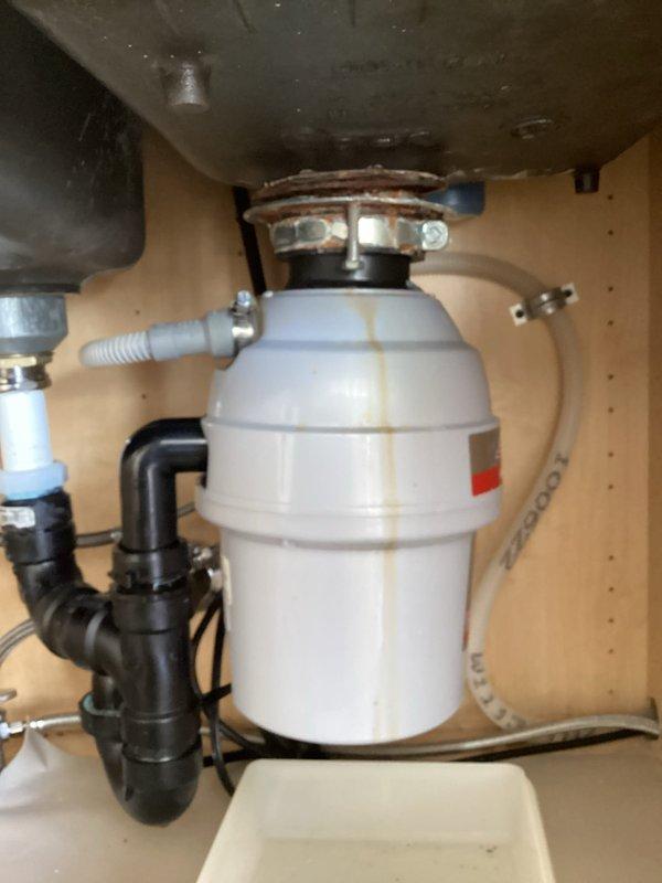 Responded to service call for leaking garbage disposal seal beneath cast iron sink. Upon inspection, identified compromised seal at mounting assembly connection point between disposal unit and sink drain. Evaluated condition of existing white cylindrical disposal unit, including mounting hardware, brackets, and connection integrity. Assessed P-trap configuration and associated black PVC drainage components for proper alignment and function. Photographed installation showing disposal mounting, plumbing connections, and undermount sink with chrome fixtures. Discussed repair versus replacement options with customer based on unit age and seal condition. Appointment rescheduled to accommodate customer availability for completion of selected repair solution.