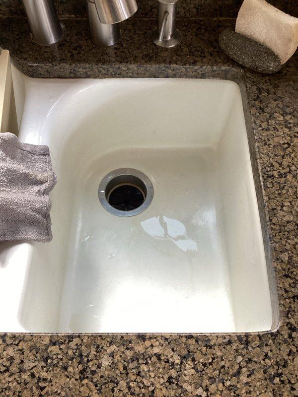 Responded to service call for leaking garbage disposal seal beneath cast iron sink. Upon inspection, identified compromised seal at mounting assembly connection point between disposal unit and sink drain. Evaluated condition of existing white cylindrical disposal unit, including mounting hardware, brackets, and connection integrity. Assessed P-trap configuration and associated black PVC drainage components for proper alignment and function. Photographed installation showing disposal mounting, plumbing connections, and undermount sink with chrome fixtures. Discussed repair versus replacement options with customer based on unit age and seal condition. Appointment rescheduled to accommodate customer availability for completion of selected repair solution.