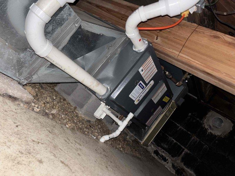 Completed comprehensive evaluation of existing HVAC air handler unit located in crawl space for equipment replacement estimate. Assessed current system configuration including air handler positioned on floor joists, refrigerant line routing, electrical connections via orange conduit, and flexible ductwork installation. Documented crawl space access conditions, structural support system with concrete block pillars, moisture presence on concrete flooring, and clearance limitations for equipment replacement considerations. Photographed existing unit specifications, refrigerant line insulation condition, and surrounding installation environment to provide customer with multiple replacement options and system upgrade recommendations.