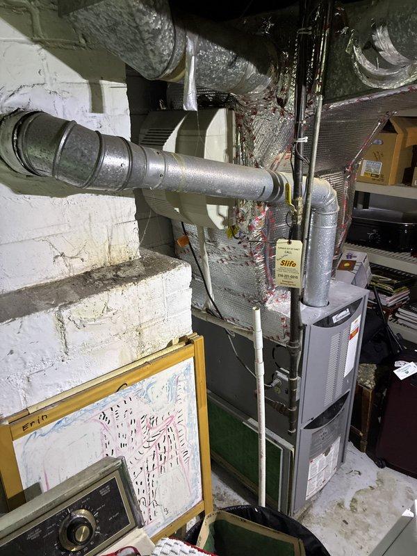 Conducted comprehensive site evaluation for HVAC system replacement at residential property. Assessed existing outdoor condenser unit with gray cylindrical housing and indoor furnace system located in basement utility area. Documented current equipment configuration including refrigerant line routing, electrical disconnect, and ductwork connections. Evaluated accessibility for replacement work, noting adequate clearance around outdoor unit despite vegetation growth near foundation. Inspected basement installation space with vertical furnace mounted against concrete block wall and flexible ductwork distribution system. Provided customer with multiple replacement options including AC-only upgrade and complete system replacement packages. Photographed existing equipment conditions and installation environment for proposal documentation.