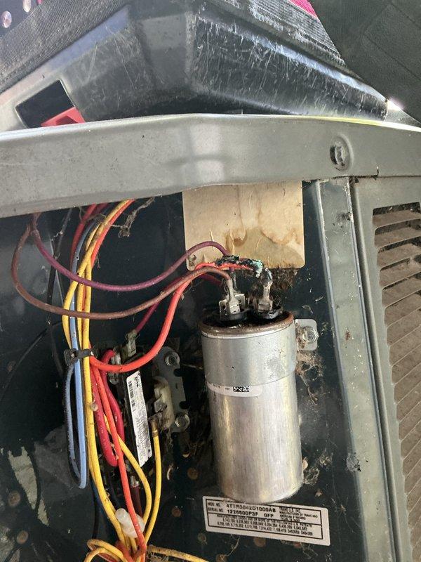 Responded to no cooling condition affecting entire residence with 10+ year old air conditioning system. Upon inspection, found outdoor unit electrical compartment with significant accumulation of organic debris, dirt, and fibrous material in lower housing area. Assessed capacitor condition showing age-related discoloration and surface contamination. Documented electrical connections including power wiring and control circuits to capacitor terminals. Unit exhibited signs of extended service life with visible wear, dirt buildup, and minor surface corrosion on interior metal housing. Photographed electrical components and debris accumulation for service records.