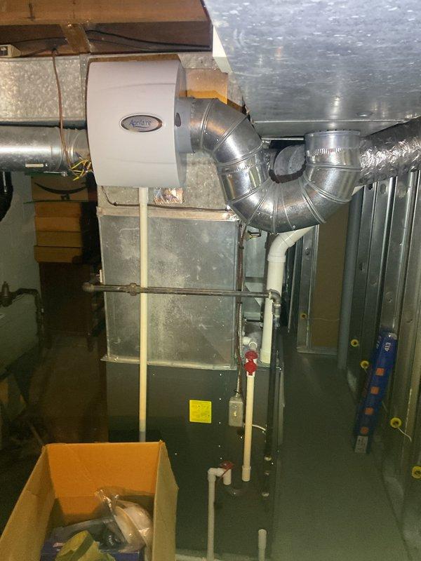 # HVAC Cooling Maintenance Completed

Performed comprehensive cooling system maintenance on residential forced-air HVAC system with Aprilaire humidifier integration. Conducted thorough inspection of basement mechanical room installation, including furnace unit, ductwork, and associated components.

## Work Performed

Inspected and evaluated main furnace cabinet and associated ductwork system. Examined metallic supply and return ducts with 90-degree elbow configurations for proper airflow and structural integrity. Verified Aprilaire whole-home humidifier mounting and connection points to main trunk line.

Assessed PVC condensate drain lines for proper pitch and drainage function. Noted discoloration and mineral buildup on cylindrical ductwork component, indicating moisture exposure or condensate issues. Documented staining patterns on Schedule 40 PVC piping with copper fittings.

Utilized digital temperature measurement device to verify system operating temperatures and performance para