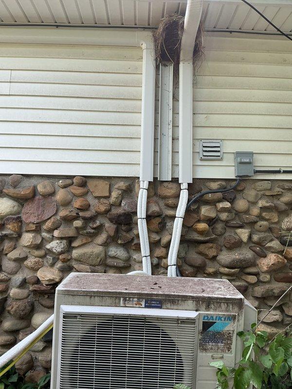 Responded to service call for Daikin split system requiring uninstallation and reinstallation due to roofing work in progress. Documented current installation condition of outdoor condenser unit mounted on composite pad against stone foundation with refrigerant lines and electrical connections running through exterior wall. Unit showed normal weathering and operational wear but no immediate mechanical concerns noted at time of inspection.