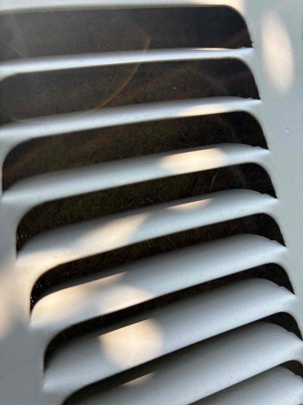 Responded to no cooling call with thermostat displaying "AC open circuit error" message. Upon inspection, found outdoor unit condenser coils with dust accumulation and compressor motor showing significant rust and corrosion on housing, indicating potential electrical or mechanical failure. Documented equipment condition through protective grille, noting deteriorated motor casing and corroded components that likely contributed to the open circuit fault detected by thermostat.
