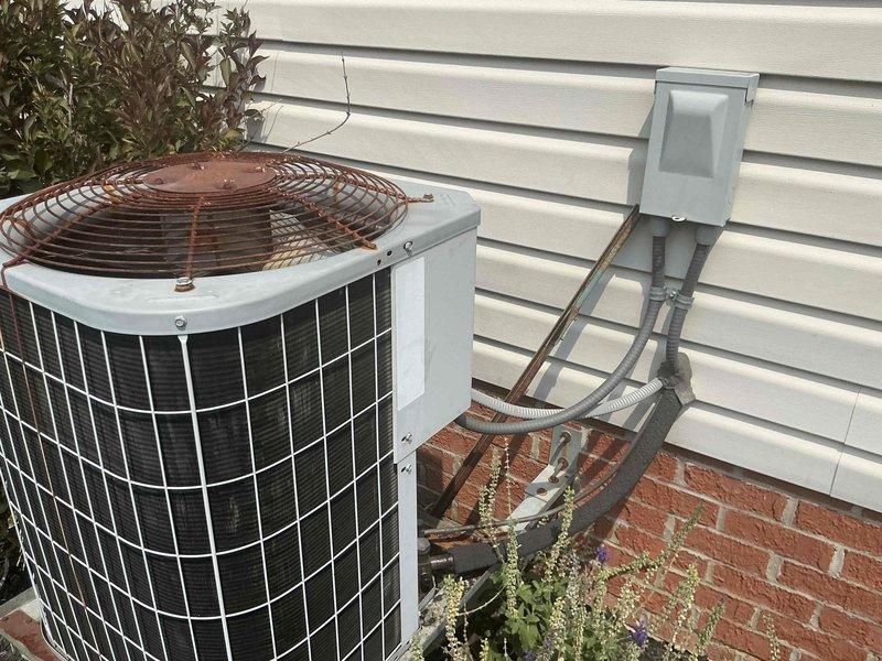 Conducted on-site evaluation of existing Carrier HVAC system consisting of 85,000 BTU furnace and 3.5-ton air conditioning unit for complete system replacement. Inspected outdoor condenser unit showing significant age-related deterioration including severe rust and corrosion on fan grille assembly, assessed electrical disconnect and conduit connections, and evaluated indoor air handler installation in mechanical room with exposed framing to determine proper equipment specifications and replacement requirements for new system installation.