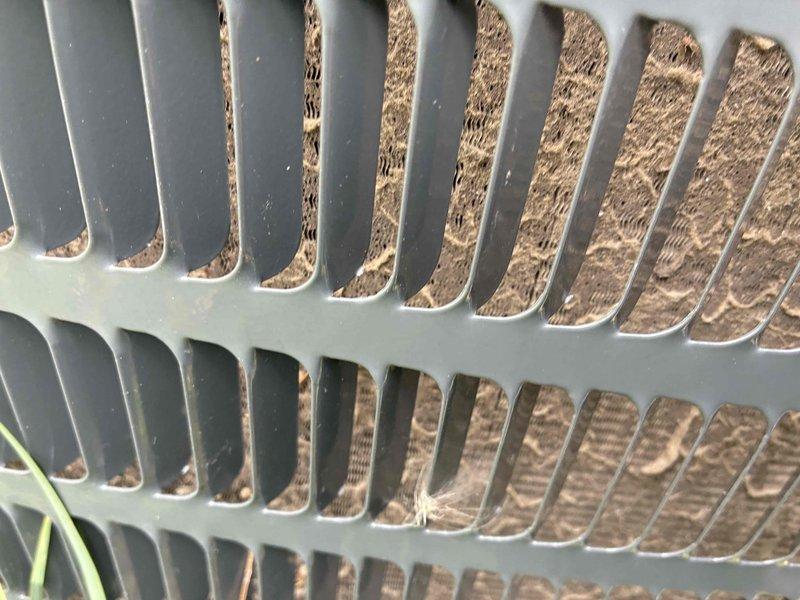 Responded to no cooling complaint on residential air conditioning system. Upon arrival, found outdoor condenser unit heavily obstructed by overgrown vegetation and debris accumulation around intake grille. Cleared dried weeds, plant material, and cotton-like seed fibers that had completely blocked airflow to the unit. Removed debris from condenser coil fins and surrounding areas to restore proper ventilation. System airflow restriction was preventing adequate heat exchange, causing loss of cooling capacity. After clearing obstruction and verifying unimpeded airflow through condenser coils, unit returned to normal operation with proper cooling restored.
