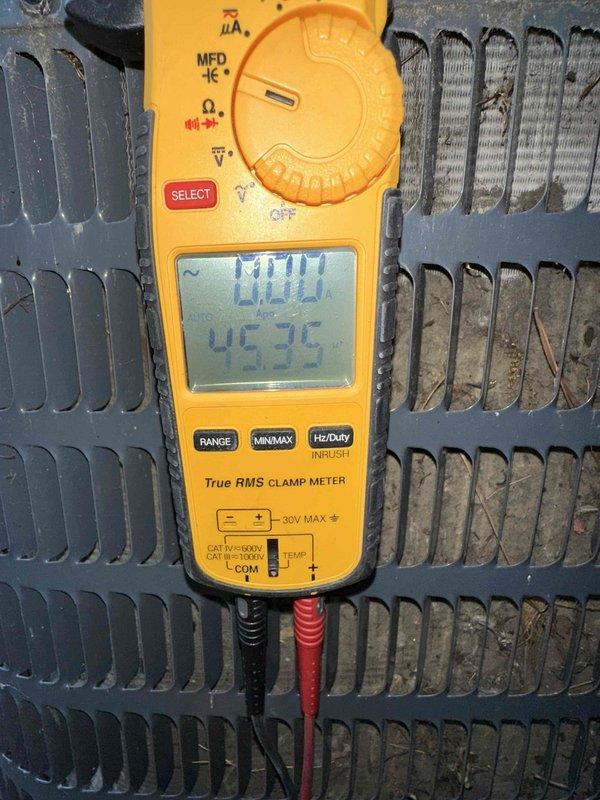 Performed comprehensive cooling season tune-up on residential air conditioning system. Conducted electrical measurements using digital clamp meter, recording temperature readings at condenser unit which showed 45.7°C. Inspected outdoor condenser unit with green metal housing, noting dust and debris accumulation on coil fins requiring attention during routine maintenance service.