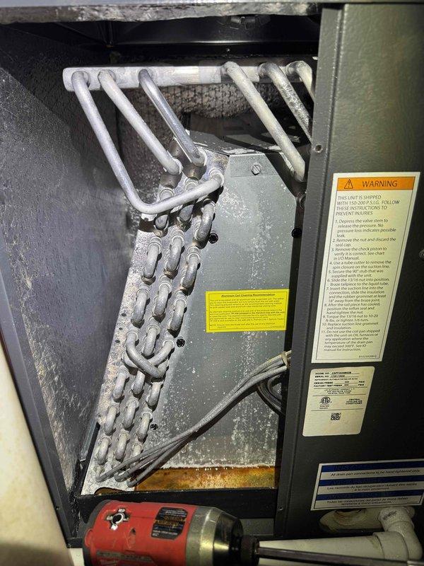 # HVAC Cooling System Maintenance with Evaporator Coil Issue

Performed scheduled cooling maintenance on residential HVAC system located in basement mechanical room. Upon initial inspection, discovered significant frost and ice accumulation on evaporator coil assembly, indicating restricted airflow or potential refrigerant issue affecting system performance.

Documented existing system condition including furnace unit, air handler cabinet, and associated ductwork and piping configurations. The heavy ice buildup on the evaporator coil's serpentine tubing required immediate attention as this condition severely impacts cooling efficiency and can lead to compressor damage if left unaddressed. Assessed unit labels and specifications to verify proper system operation parameters and identify potential causes of the icing condition, which typically results from reduced airflow across the coil, low refrigerant charge, or thermostat issues.

Completed comprehensive cooling system evaluation as p