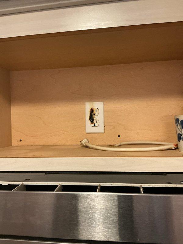 Responded to service call for non-functioning kitchen outlet. Upon arrival, inspected electrical receptacle located in cabinet space above range hood. Tested outlet for power, verified proper wiring connections, and documented existing conditions with photographs showing outlet installation within cabinet interior above KitchenAid appliance.