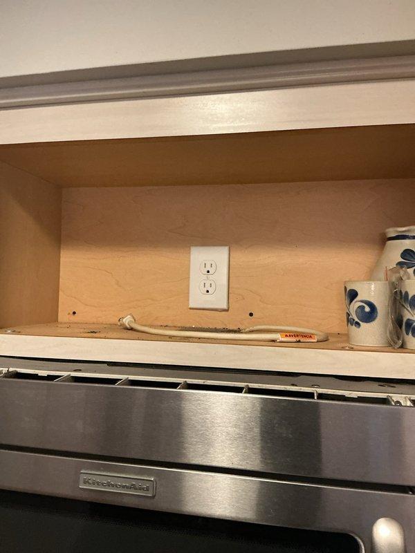 Responded to service call for non-functioning kitchen outlet. Upon arrival, inspected electrical receptacle located in cabinet space above range hood. Tested outlet for power, verified proper wiring connections, and documented existing conditions with photographs showing outlet installation within cabinet interior above KitchenAid appliance.