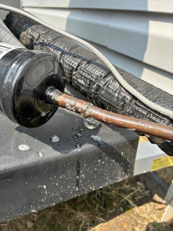 # HVAC Maintenance - Cooling System Inspection and Documentation

Performed comprehensive contract fulfillment inspection on outdoor cooling system unit. Conducted thorough visual assessment of all accessible components including compressor housing, refrigerant lines, electrical connections, and mounting hardware. Documented current system condition through photographic evidence for maintenance records.

During inspection, identified significant corrosion and rust buildup on copper refrigerant line extending from compressor motor housing. Noted deterioration of copper pipe surface with reddish-brown patina indicating prolonged moisture exposure. Observed water droplets and condensation on metal surfaces surrounding unit, consistent with normal system operation.

Critical finding: Discovered pinhole leak at refrigerant line connection point. Isolated and documented the compromised fitting showing blue and yellow refrigerant line connections. This leak represents a system integrity issue