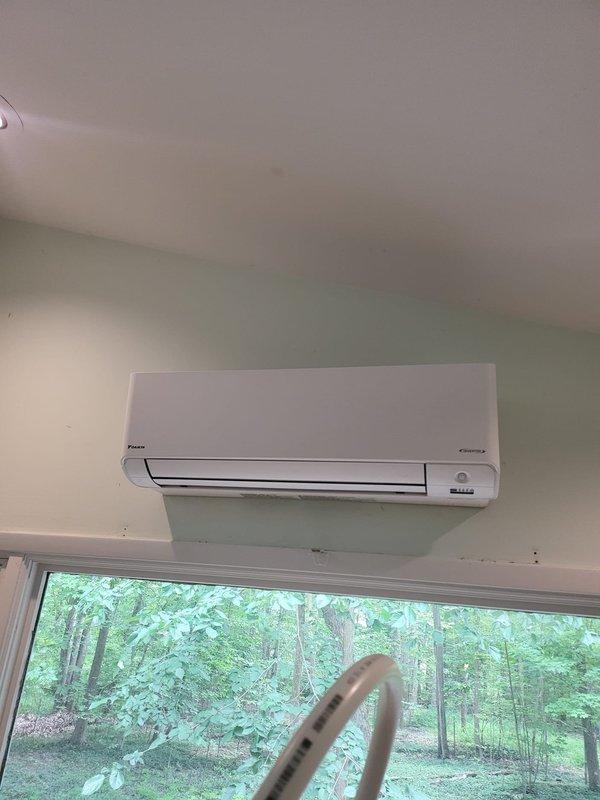 Completed installation of Daikin ductless mini-split system at residential property. Mounted outdoor condenser unit on wooden deck and installed indoor wall-mounted air handler above window in living space, running refrigerant lines and electrical connections between units. System tested and confirmed operational upon completion.