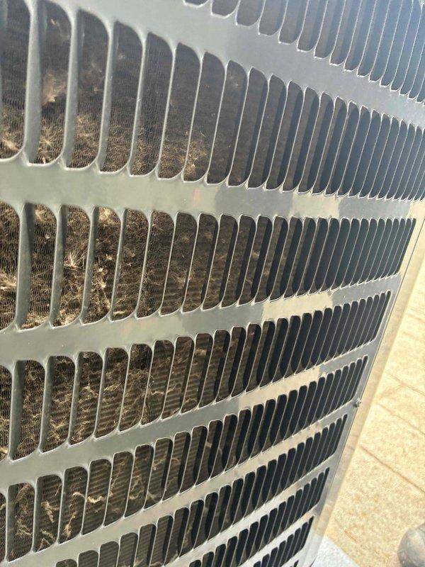 Completed scheduled cooling system maintenance on outdoor HVAC condenser unit. Performed thorough inspection of condenser coil assembly, which revealed significant accumulation of dirt, dust, and organic debris between aluminum fins. Cleaned condenser coils to restore proper airflow and heat transfer efficiency. Verified protective metal grille structural integrity and confirmed unit operational status upon completion.