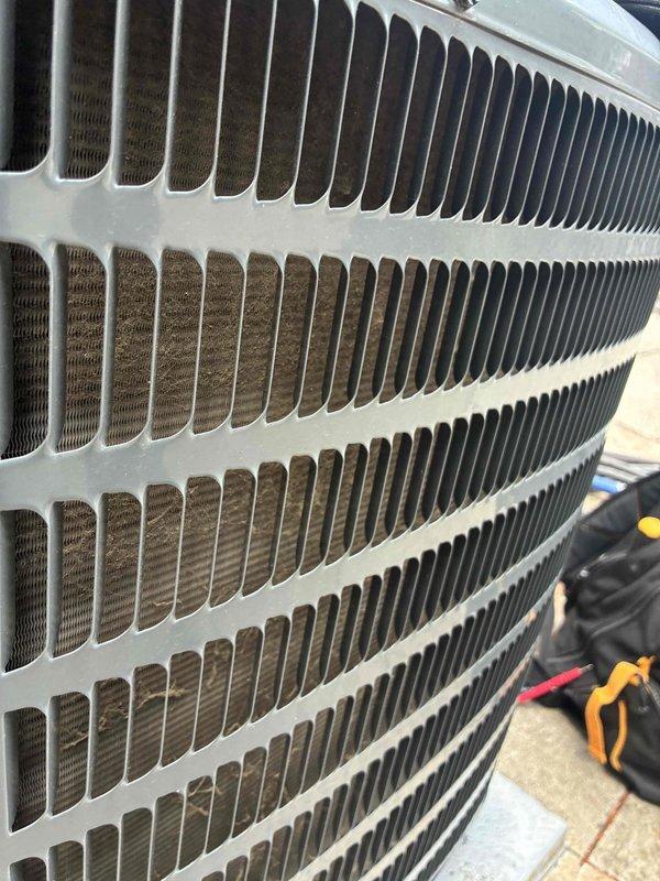 Completed scheduled cooling system maintenance on outdoor HVAC condenser unit. Performed thorough inspection of condenser coil assembly, which revealed significant accumulation of dirt, dust, and organic debris between aluminum fins. Cleaned condenser coils to restore proper airflow and heat transfer efficiency. Verified protective metal grille structural integrity and confirmed unit operational status upon completion.