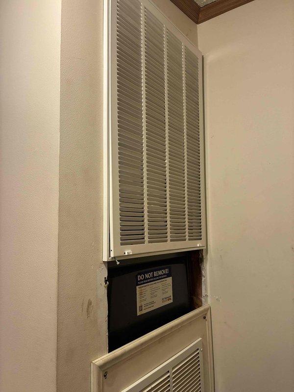 Completed preventive maintenance on wall-mounted HVAC cooling system, inspecting evaporator coil unit and ventilation components. Accessed interior service panel to verify equipment specifications and confirm proper installation of protected coil assembly with intact factory wrapping. All components operating within normal parameters upon completion of maintenance procedures.