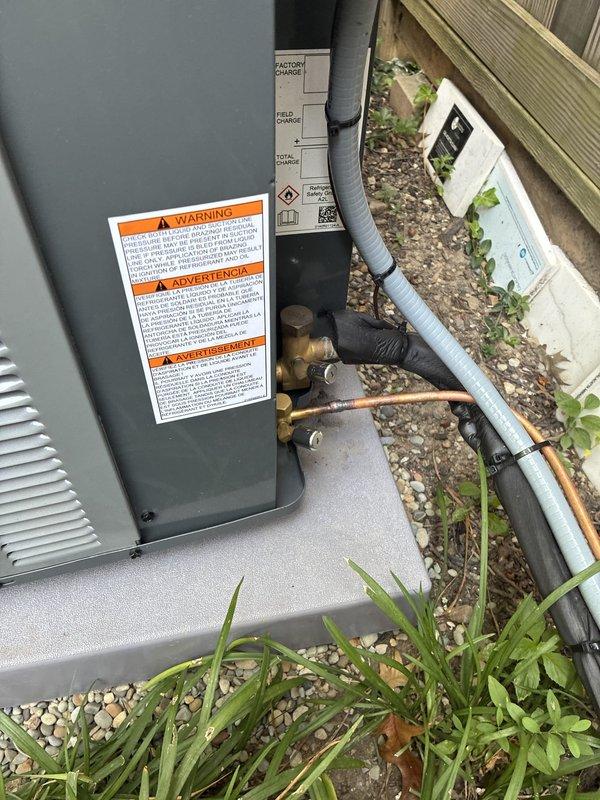 Completed warranty follow-up on recent HVAC installation by securing the control board cover that had been left on the attic floor near the air handler and tightening loose tamper-resistant caps on the outdoor condenser unit. Documentation photos were captured of both the attic-mounted air handler with associated ductwork and the ground-level condenser unit to verify completion of corrective measures.