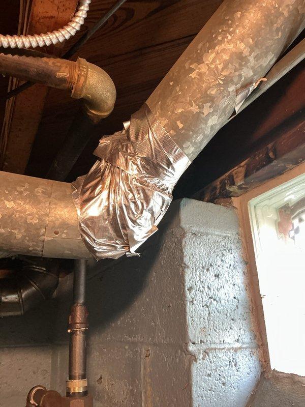 Responded to service call regarding deteriorated foil tape on AC ductwork insulation. Upon inspection, found large rectangular supply duct in basement with reflective foil wrapping showing significant wear and exposed sections where metallic tape had failed. Re-secured foil insulation wrapping with new metallic HVAC tape to restore proper vapor barrier and maintain system efficiency.
