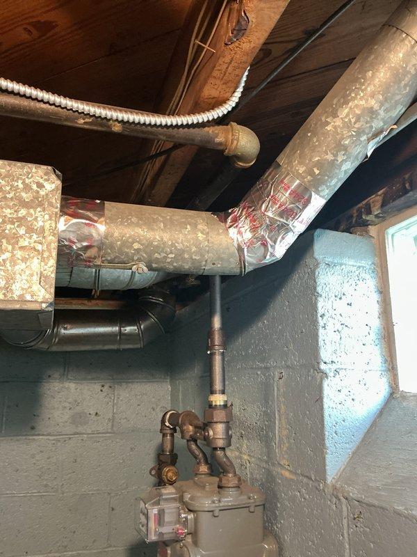 Responded to service call regarding deteriorated foil tape on AC ductwork insulation. Upon inspection, found large rectangular supply duct in basement with reflective foil wrapping showing significant wear and exposed sections where metallic tape had failed. Re-secured foil insulation wrapping with new metallic HVAC tape to restore proper vapor barrier and maintain system efficiency.