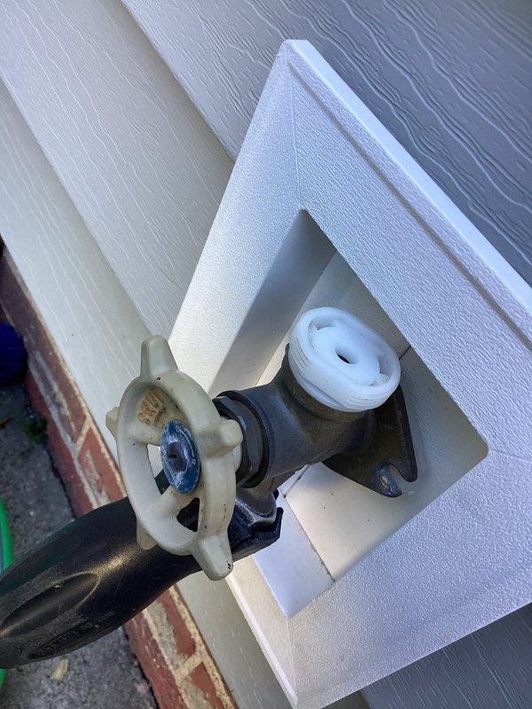 Responded to service call for non-functional outdoor hose bib mounted on exterior vinyl siding. Upon inspection, assessed the existing spigot assembly including brass valve with cross-handle control, mounting configuration through white trim plate, and connection to black rubber hose coupling. Documented current condition of fixture showing signs of weathering and age on valve components, foam insulation sleeve around pipe connection for freeze protection, and overall installation integrity. Photographed spigot assembly, mounting area, and surrounding siding to provide visual documentation for replacement quote preparation.