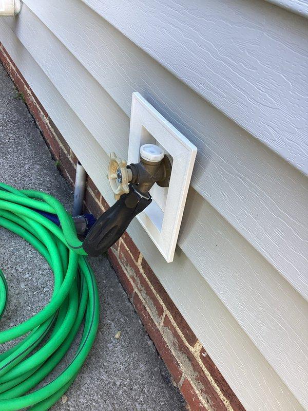 Responded to service call for non-functional outdoor hose bib mounted on exterior vinyl siding. Upon inspection, assessed the existing spigot assembly including brass valve with cross-handle control, mounting configuration through white trim plate, and connection to black rubber hose coupling. Documented current condition of fixture showing signs of weathering and age on valve components, foam insulation sleeve around pipe connection for freeze protection, and overall installation integrity. Photographed spigot assembly, mounting area, and surrounding siding to provide visual documentation for replacement quote preparation.