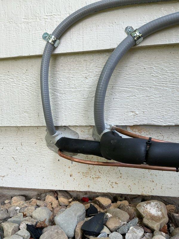 Sealed entry points for new A/C line sets on exterior wall using silicone to prevent air and moisture infiltration. Line sets were properly secured with metal clamps and routed along the building exterior, with all wall penetrations sealed to ensure energy efficiency and protect against pest entry.