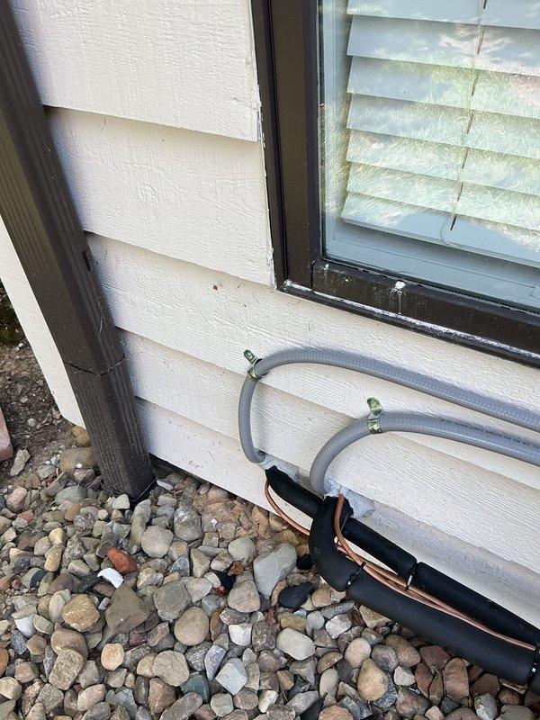 Sealed entry points for new A/C line sets on exterior wall using silicone to prevent air and moisture infiltration. Line sets were properly secured with metal clamps and routed along the building exterior, with all wall penetrations sealed to ensure energy efficiency and protect against pest entry.