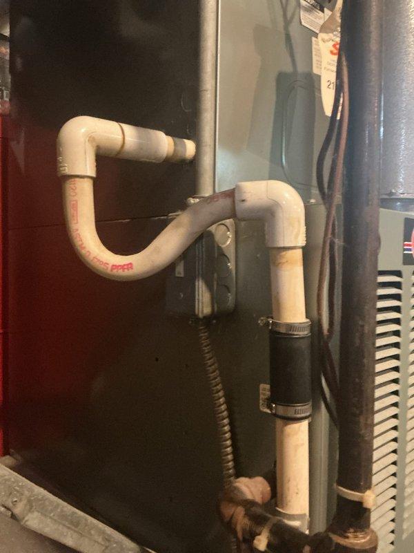 # HVAC Service Call - AC Water Leak Resolution

Responded to service call for air conditioning unit experiencing water leakage. Unit is approximately 7 years old, located at exterior installation.

Upon arrival, conducted thorough inspection of the condensing unit and associated drainage system. Examined refrigerant line configuration, noting aged copper tubing with oxidation consistent with system age. Inspected condensate drainage assembly, including white PVC piping with 90-degree elbow joints and black flexible corrugated drain line secured with hose clamps.

Identified condensate drain system as source of water leak. Checked drain line for proper pitch and blockages. Inspected drain pan and overflow connections. Verified condensate pump operation where applicable.

Cleared condensate drain line obstruction and ensured proper drainage flow. Tested system operation to confirm leak was resolved. Verified all drain connections were secure and properly sealed. Confirmed condensate was 
