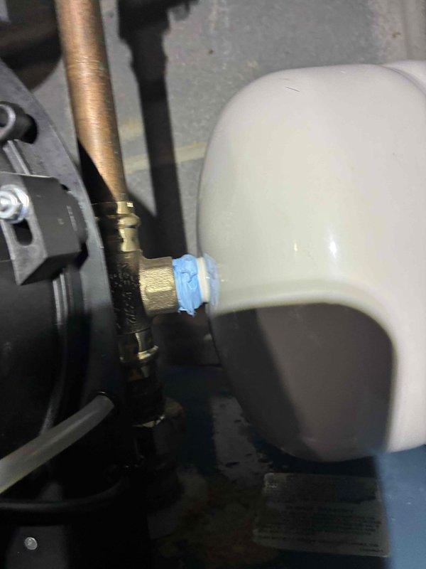 Completed water heater repair service involving the replacement of a faulty valve and installation of an expansion tank to protect the system from thermal expansion pressure. The new brass valve assembly was installed with proper copper pipe connections, and a white expansion tank was mounted and integrated into the plumbing system with appropriate fittings and connectors to ensure optimal performance and code compliance.